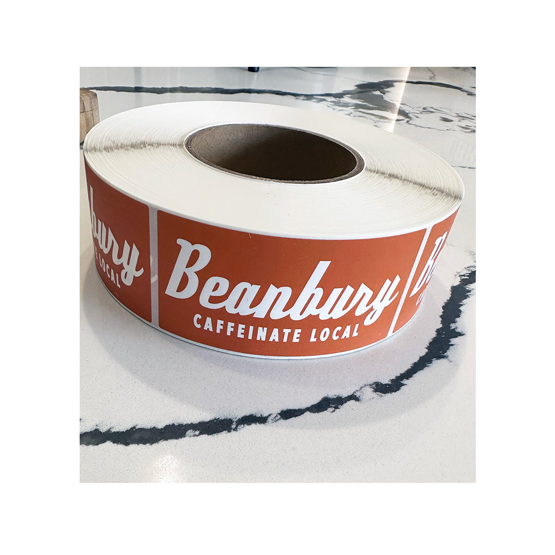 Roll of custom rectangle labels for Beanbury Coffee, printed on white BOPP with orange background and bold white logo