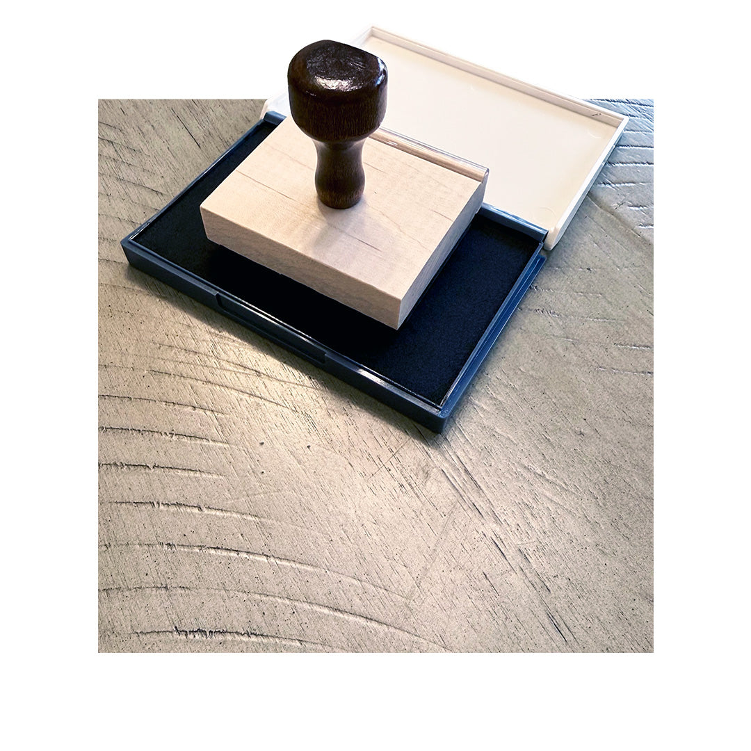 Traditional rubber stamp on open black ink pad, sitting on textured wood table