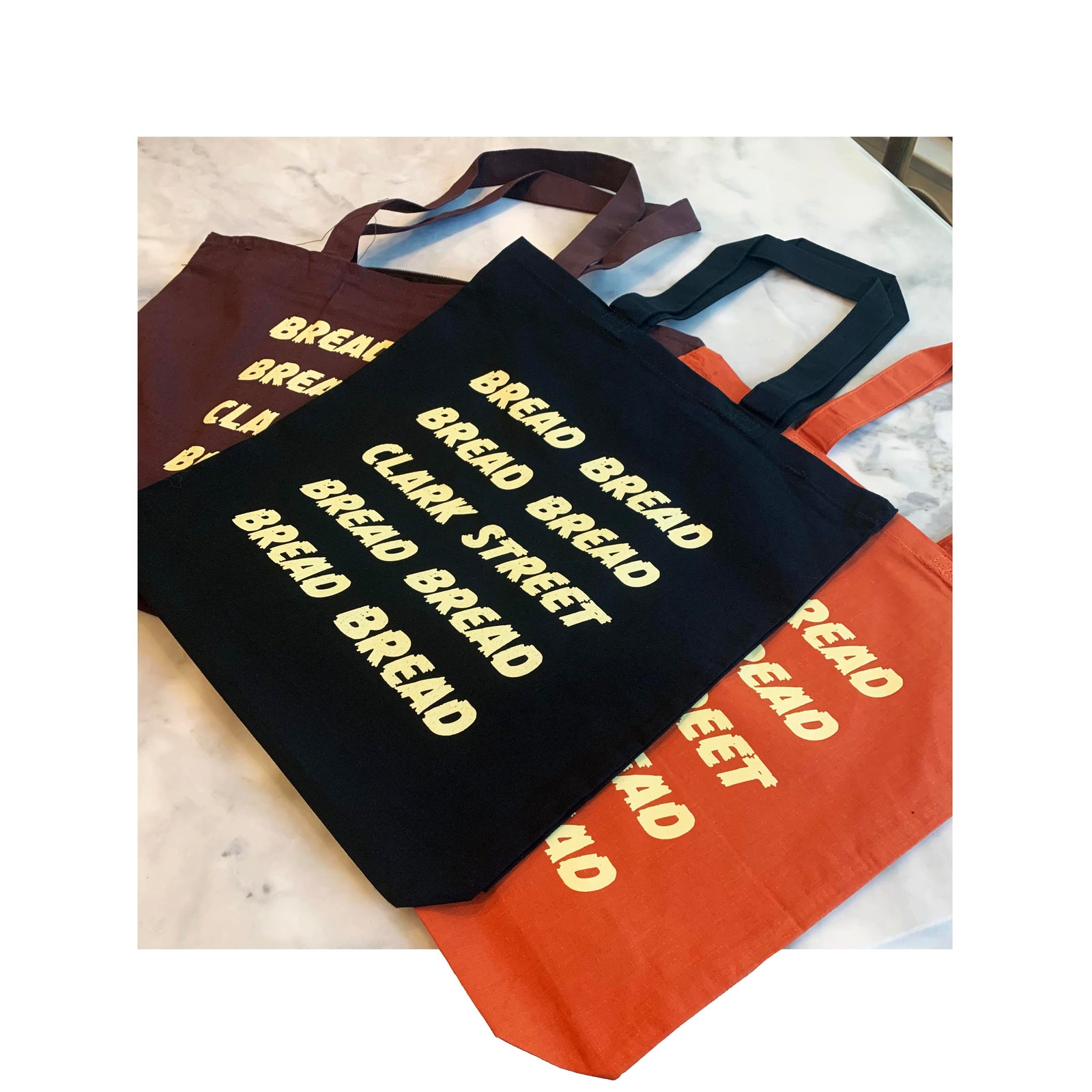 Set of colorful canvas tote bags with bold 'BREAD BREAD CLARK STREET' print in cream ink