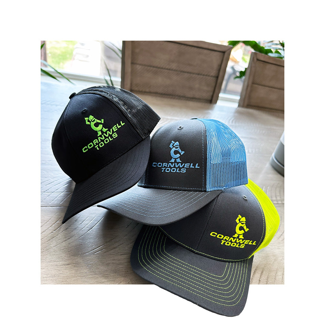 Three Richardson 112 hats with Cornwell Tools embroidery, featuring mesh backs in black, blue, and neon yellow, displayed indoors with plants in the background