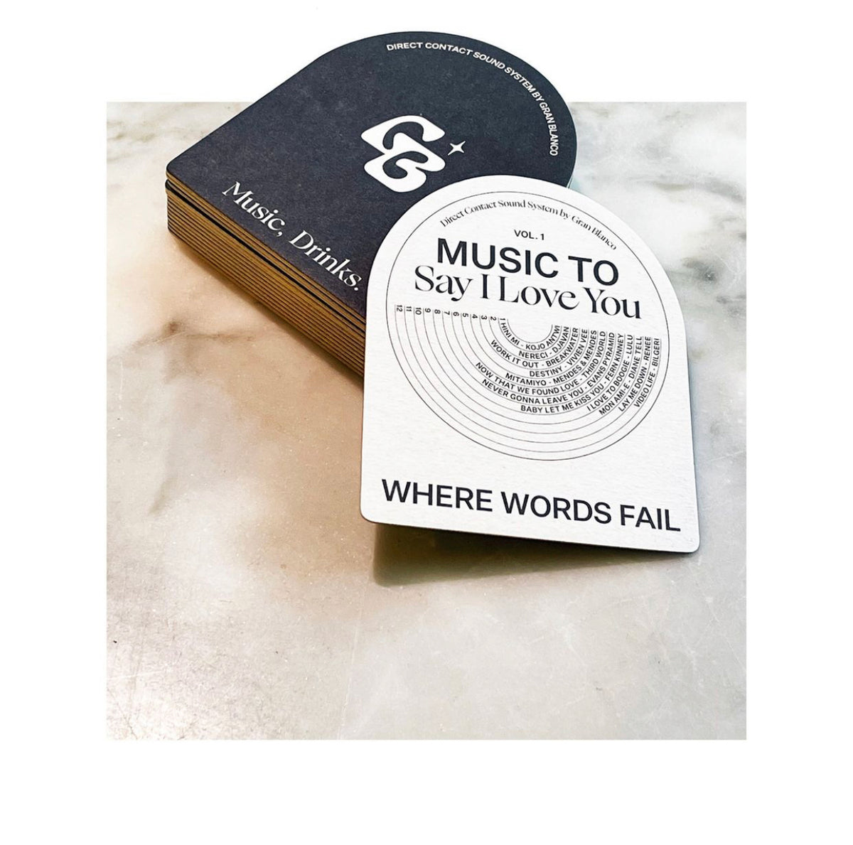 Stack of custom arched coasters featuring the Grand Blanco logo and a “Music to Say I Love You” playlist design with the phrase “Where Words Fail” printed at the bottom, displayed on a marble surface