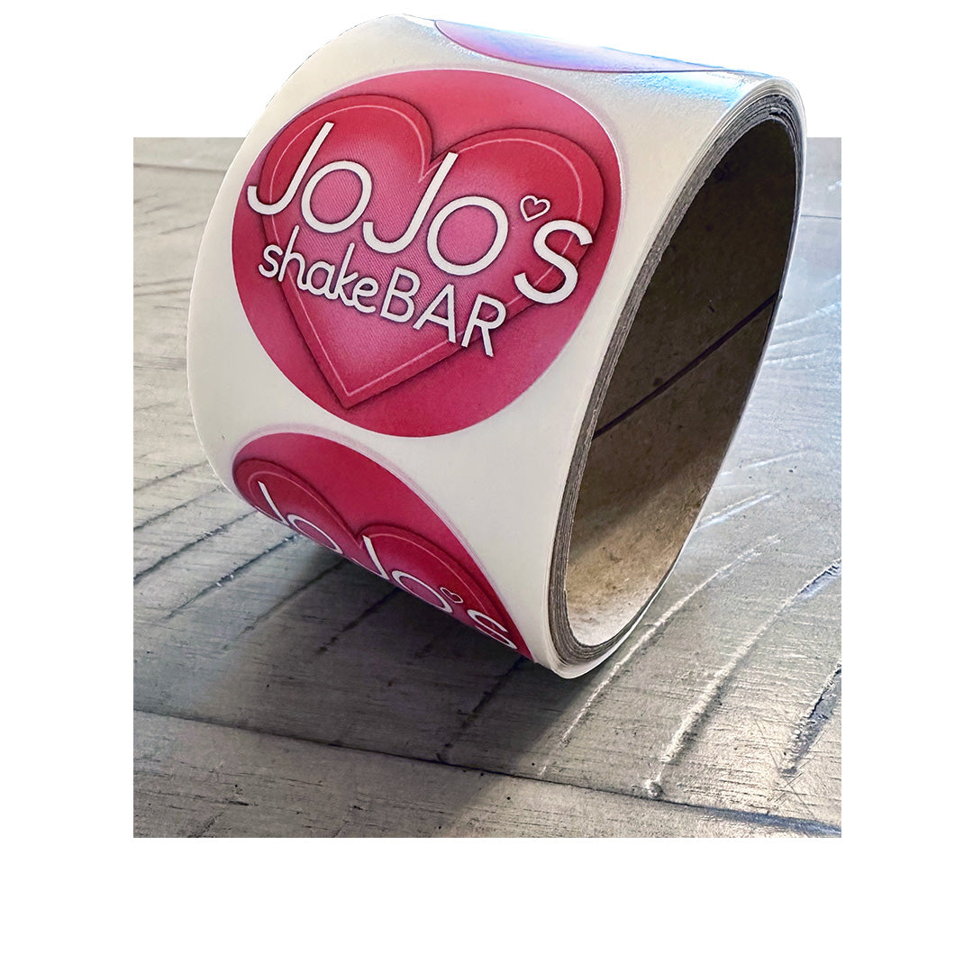 Roll of custom circle labels for JoJo’s Shake Bar with pink heart design, printed on white BOPP with gloss finish