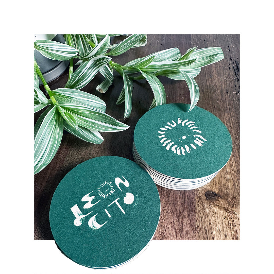 Custom printed round coasters with white ink on dark green stock, featuring restaurant logo for Leoncito
