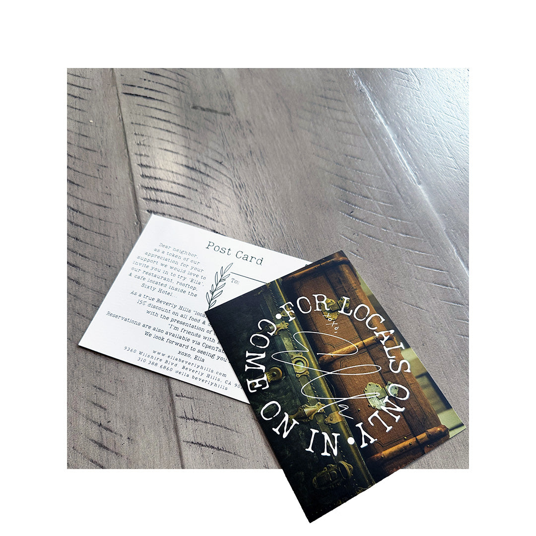 Double-sided postcard placed on a textured wooden surface. One side reads "FOR LOCALS ONLY – COME ON IN" in bold white text over a moody, rustic photo. The other side features a personalized invitation message and address details in a typewriter-style font