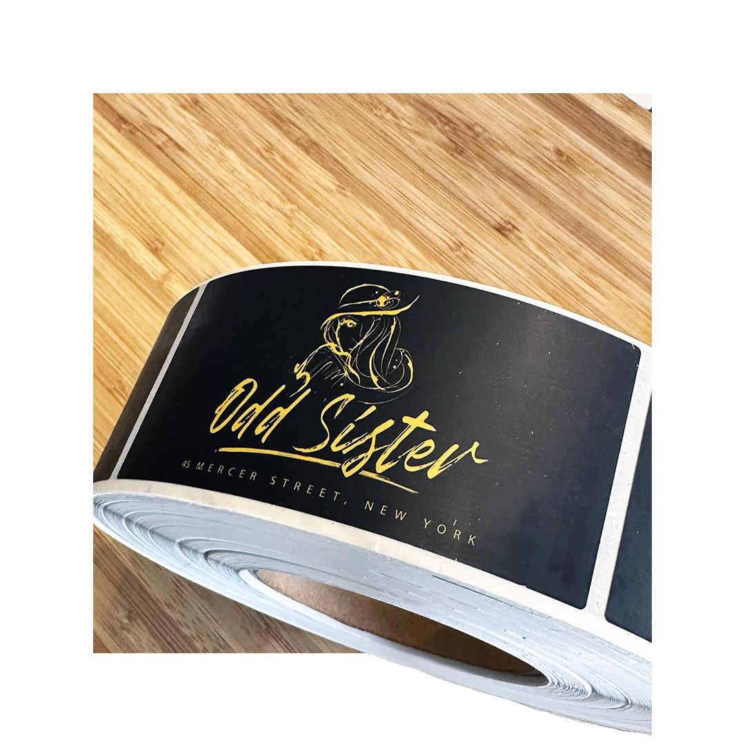 Roll of custom rectangle labels for Odd Sister boutique, featuring gold foil-style artwork on black background, printed on white BOPP