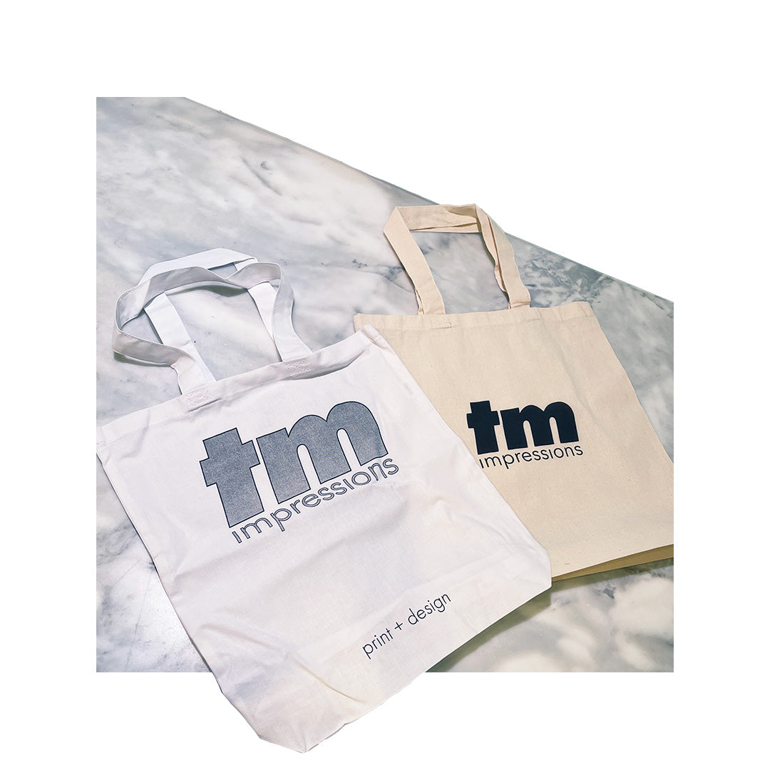 Two canvas tote bags with 'tm impressions' logo in black and gray ink on natural cotton