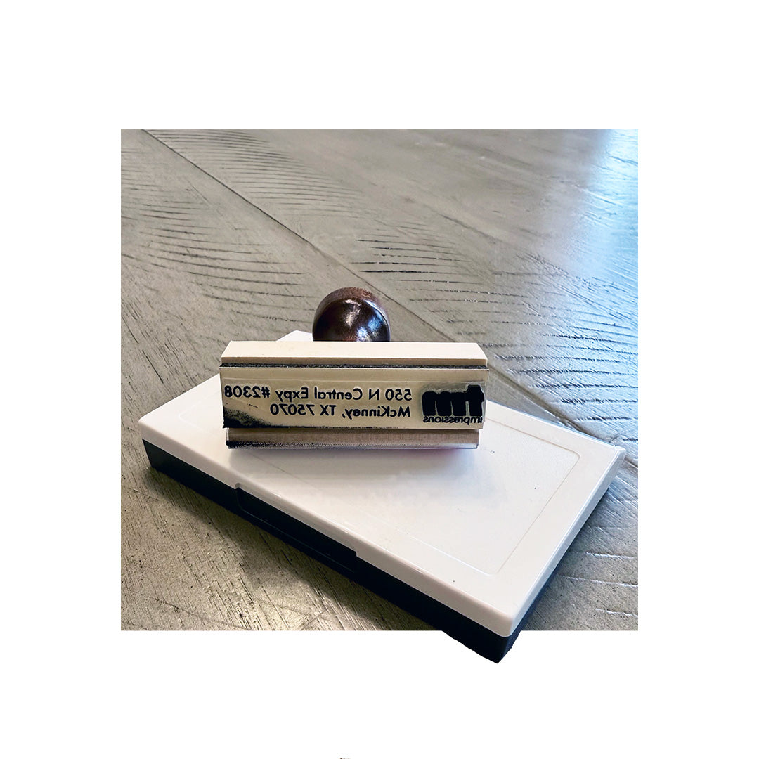 Custom rubber stamp resting on ink pad, showing printed TM Impressions return address