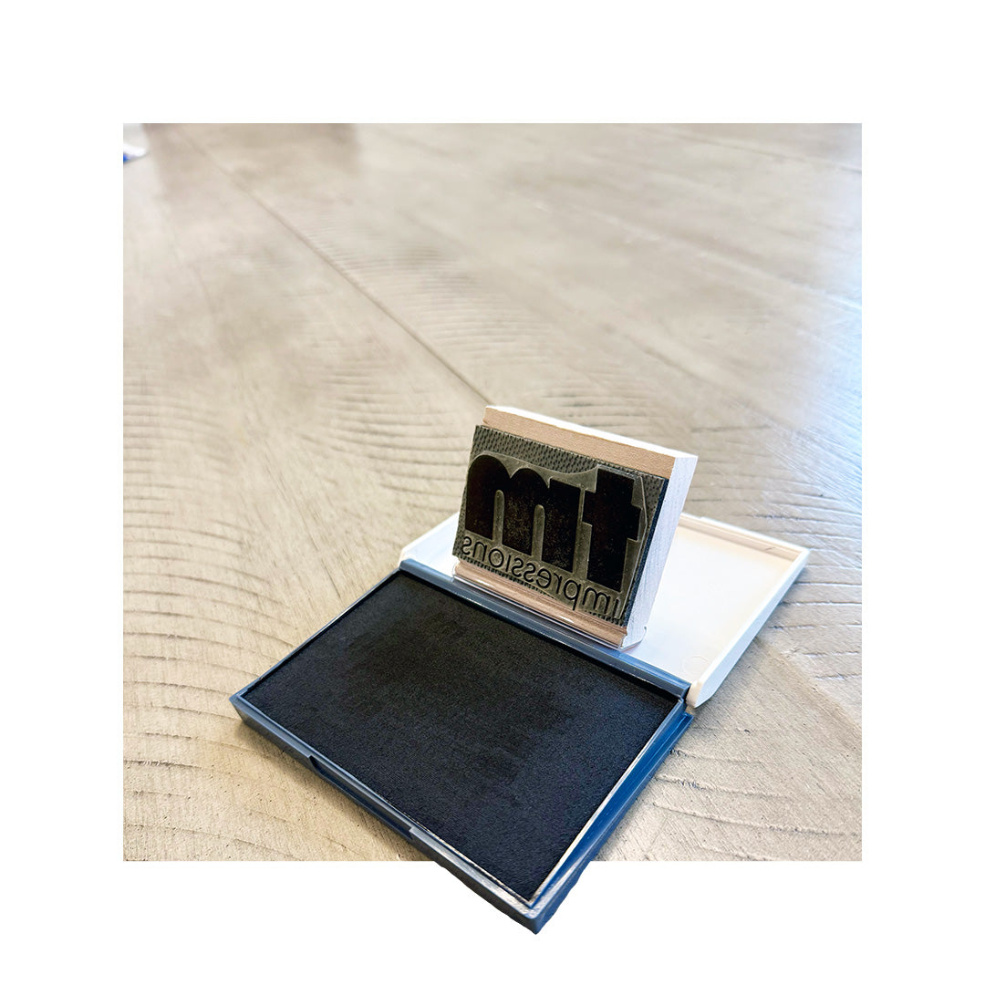 Custom TM Impressions rubber stamp angled above ink pad, showing engraved design