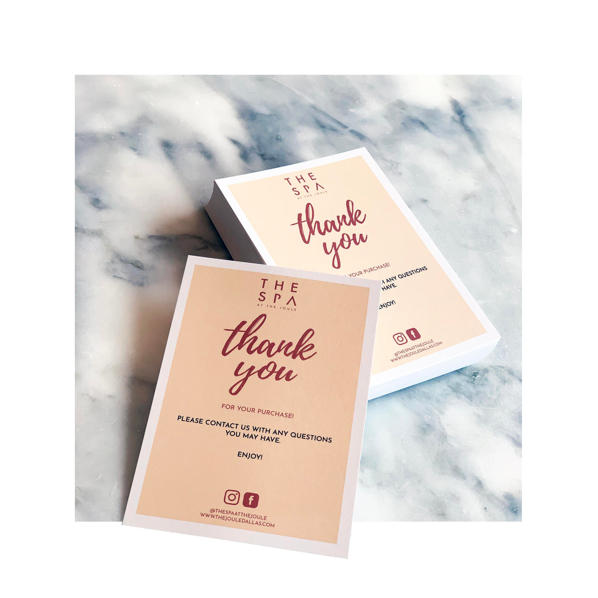 Stack of peach-toned thank-you postcards with burgundy script reading “thank you” from The Spa at The Joule, displayed on a marble surface with one postcard facing up and another stack shown in the background