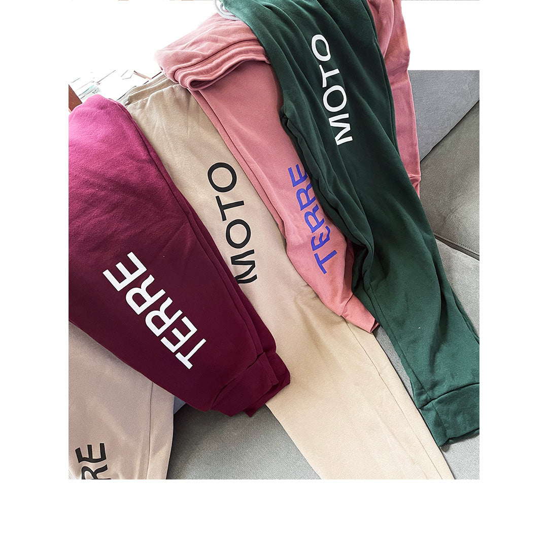 Stack of colorful Bella Canvas 3727 sweatpants in burgundy, beige, pink, and green with “TERRE” and “MOTO” text down the legs