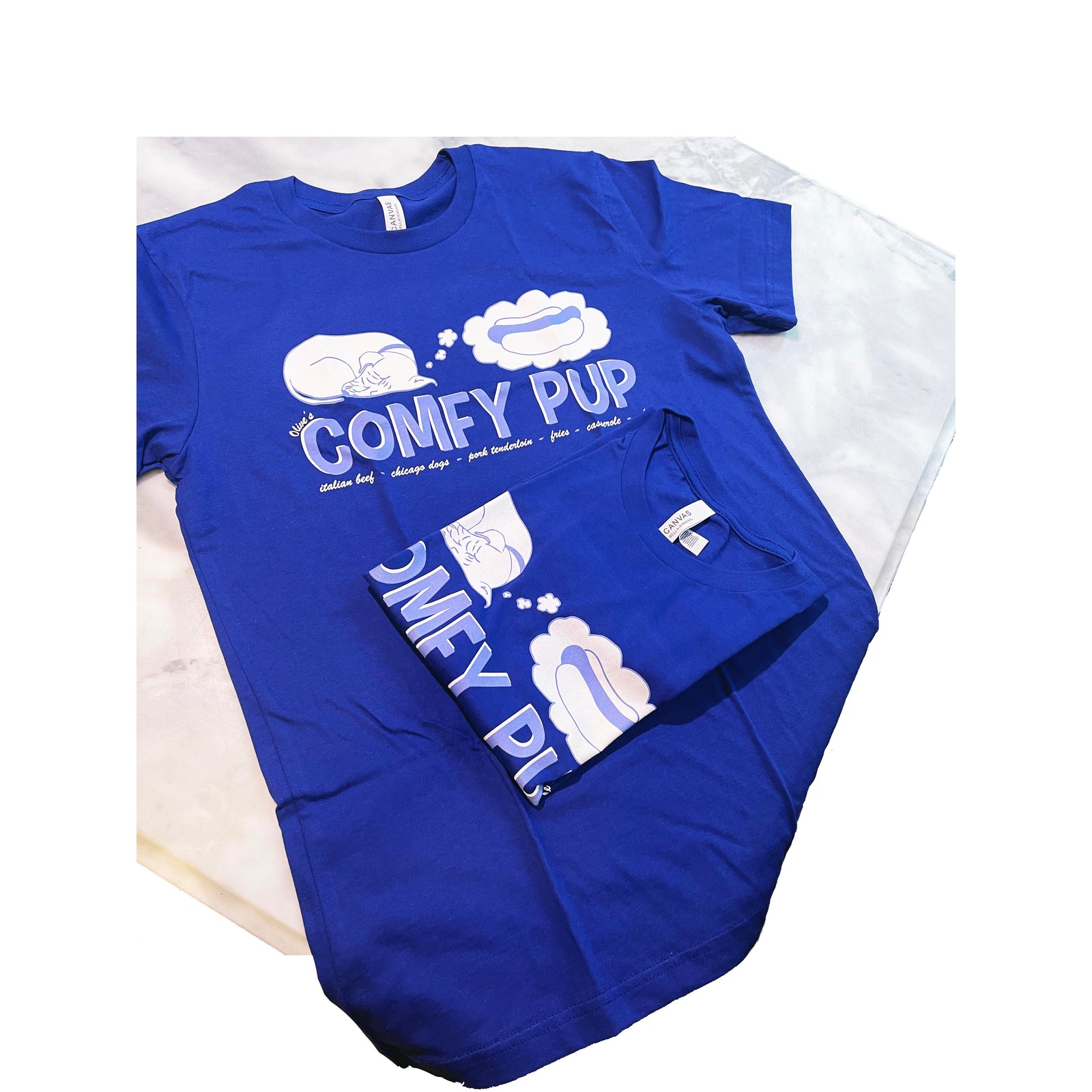 Two royal blue Bella Canvas 3001 t-shirts with custom Comfy Pup branding in white and light blue, featuring a cartoon dog graphic