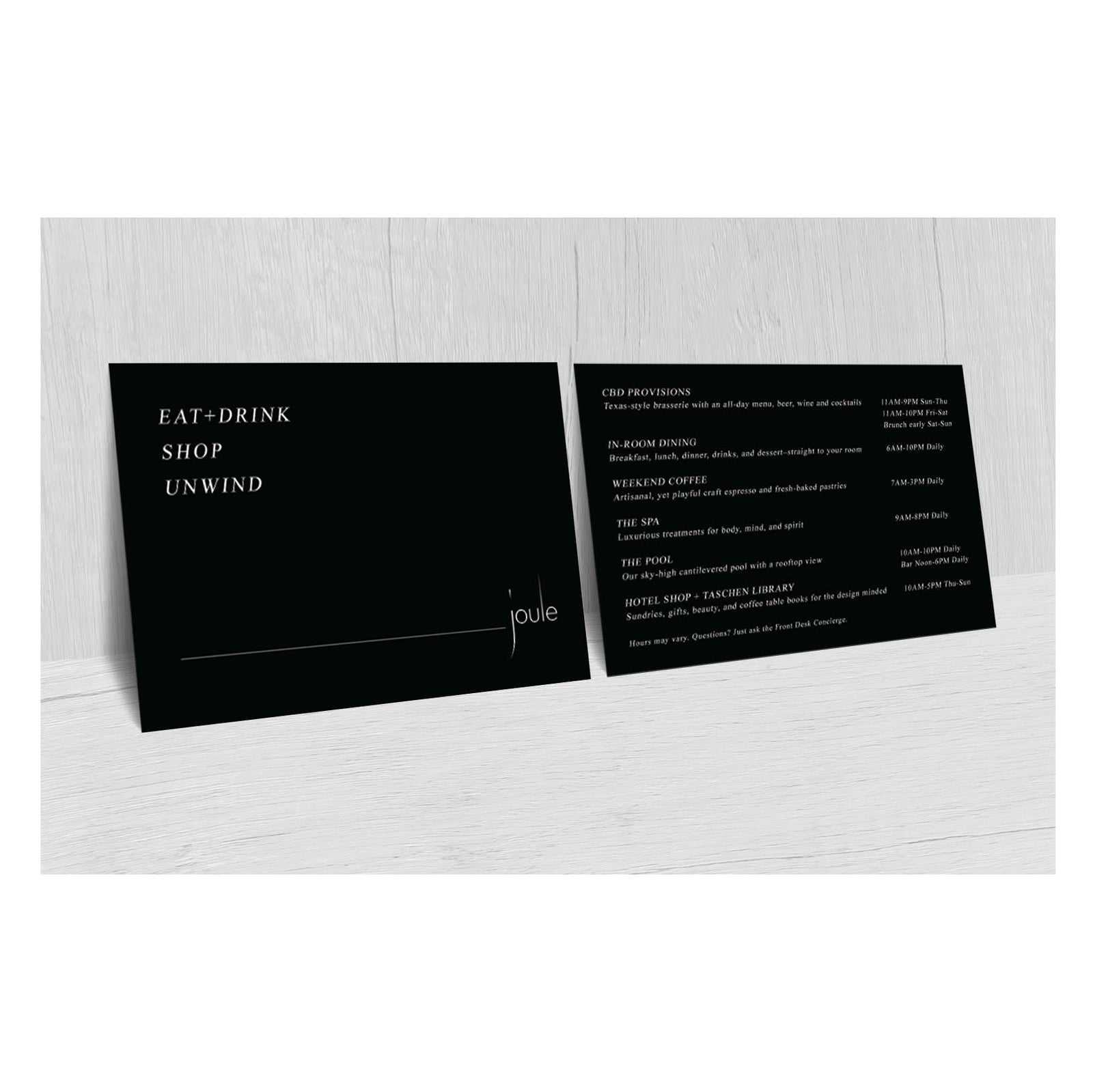 Double-sided black postcard for The Joule hotel. One side reads “EAT + DRINK, SHOP, UNWIND” in minimalist white text with The Joule logo in the corner. The other side lists hotel amenities including dining, spa, coffee, pool, and shop services, along with their hours of operation in small white text.
