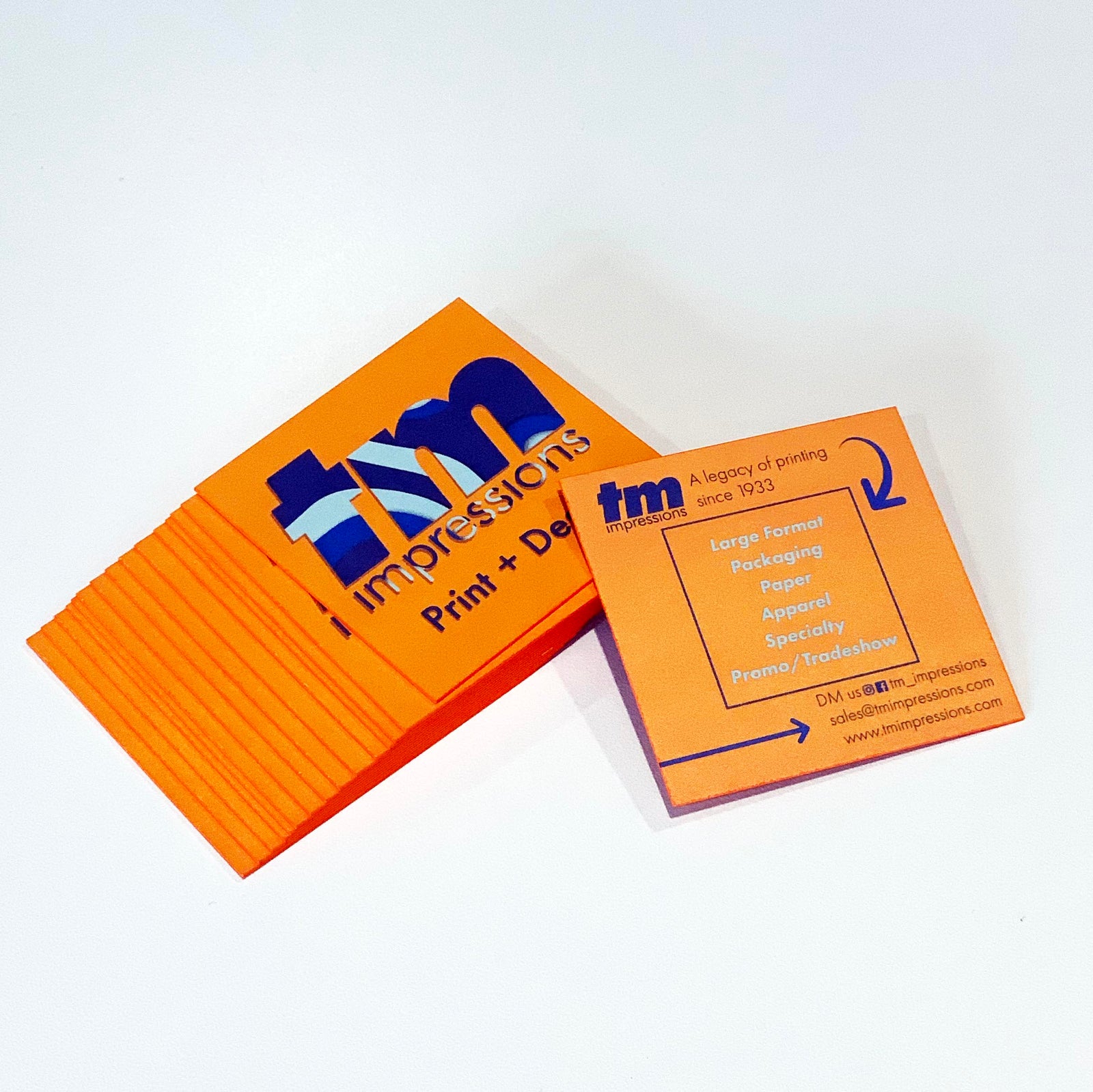 Stack of bright orange painted edge business cards with bold TM Impressions logo and contact info on back side