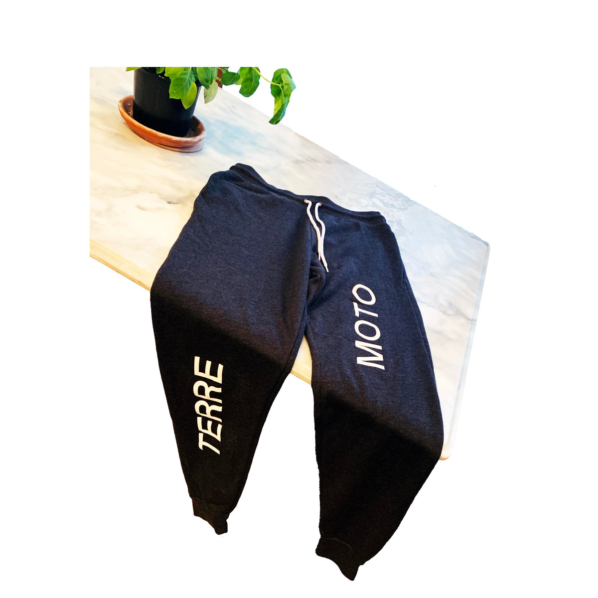 Black Bella Canvas 3727 sweatpants with “TERRE” and “MOTO” printed on opposite legs, laid flat on marble counter