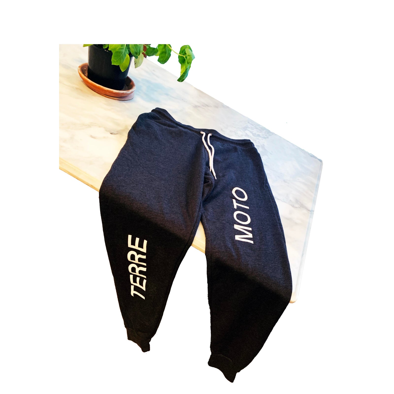 Black Bella Canvas 3727 sweatpants with “TERRE” and “MOTO” printed on opposite legs, laid flat on marble counter